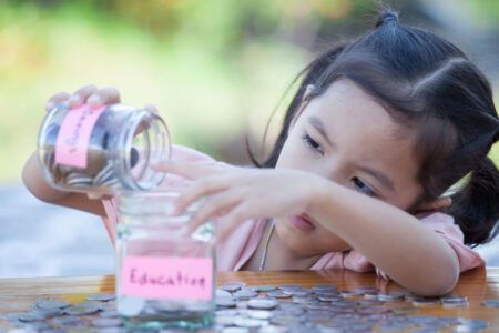 young girl putting coins into a glass jar that says education